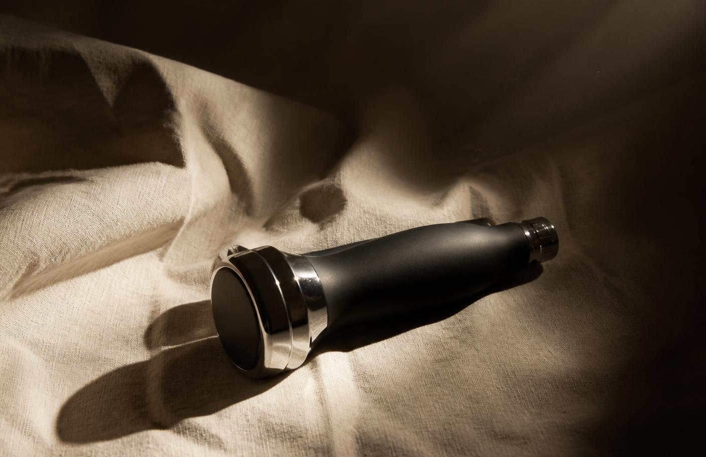 An unmarked device handpiece resting on linen under a single hard light